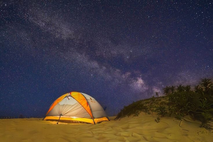 Campamento móvil en el desierto de Merzouga con tiendas instaladas sobre las dunas de arena dorada, rodeado de un cielo azul claro